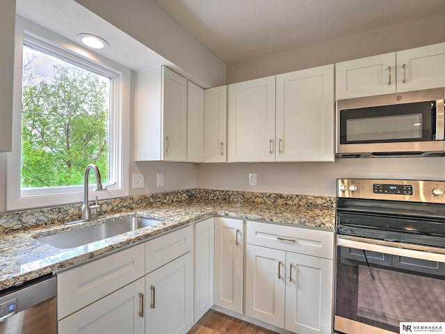 kitchen with light stone countertops, white cabinets, a sink, light wood finished floors, and appliances with stainless steel finishes