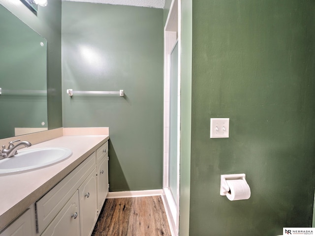 bathroom with baseboards, wood finished floors, a shower with shower door, and vanity