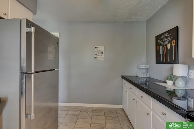 kitchen featuring freestanding refrigerator, white cabinetry, baseboards, and marble finish floor