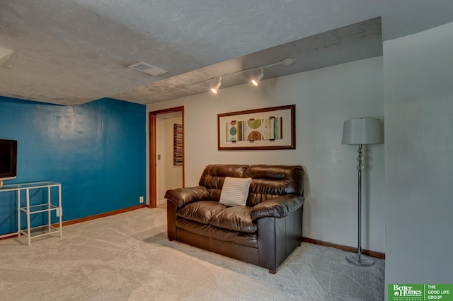 carpeted living area featuring a textured ceiling, baseboards, visible vents, and track lighting
