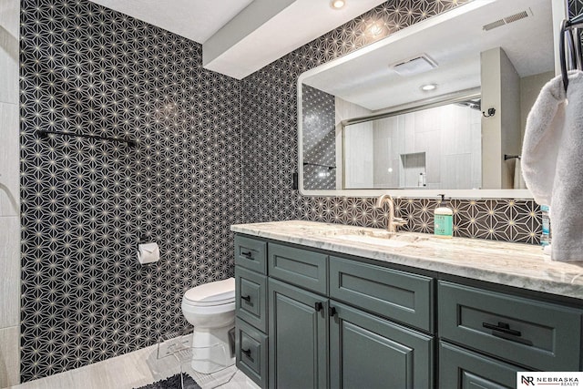 full bath featuring toilet, walk in shower, visible vents, and vanity