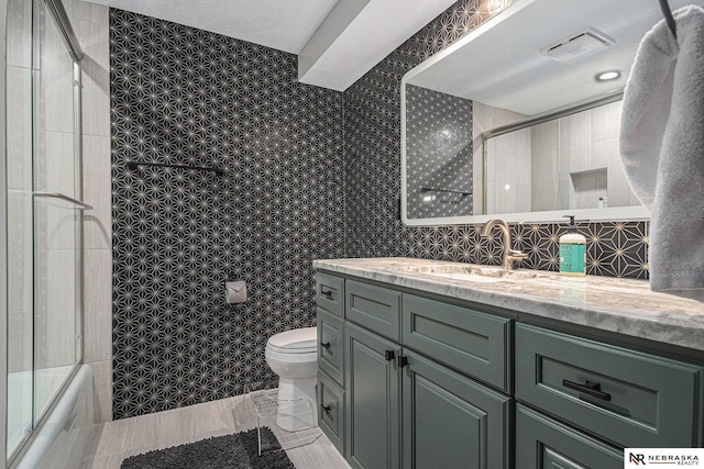 full bath with vanity, toilet, and shower / bath combination with glass door