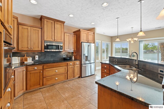 S-1007 Shady Ln, Fremont, NE 68025 - kitchen featuring stainless steel appliances, a sink, brown cabinetry, decorative backsplash, and decorative light fixtures