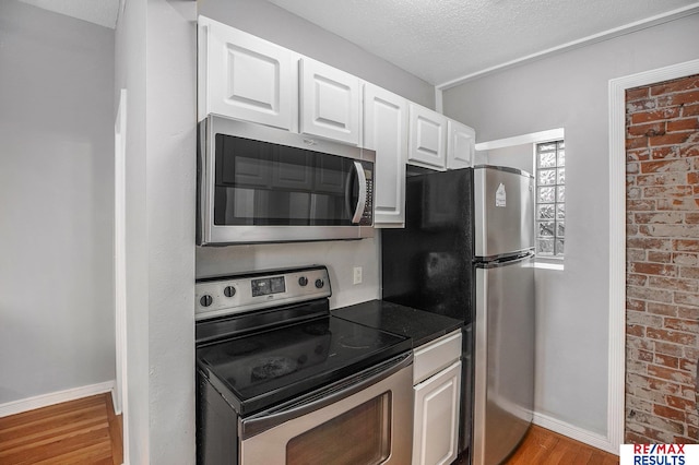 kitchen featuring a textured ceiling, dark countertops, appliances with stainless steel finishes, light wood finished floors, and white cabinetry