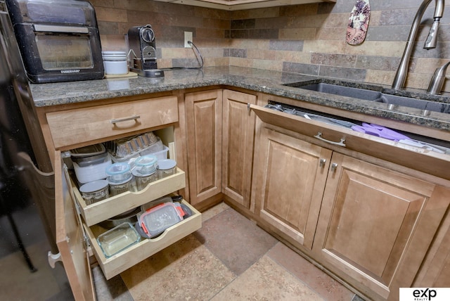kitchen with stone finish flooring, stone counters, a sink, and tasteful backsplash