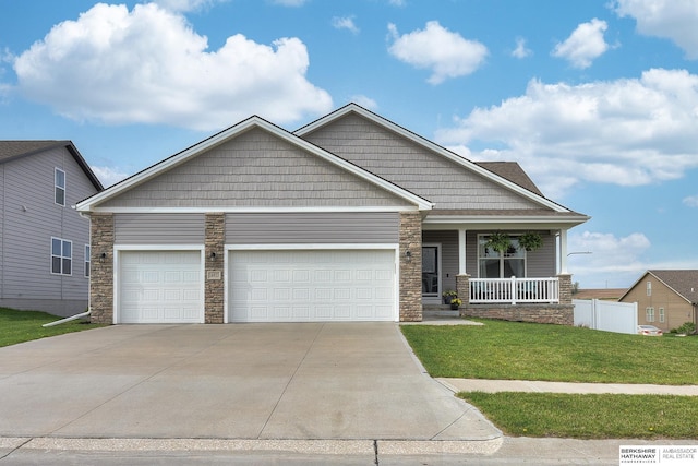 craftsman-style home with covered porch, driveway, a front yard, an attached garage, and stone siding