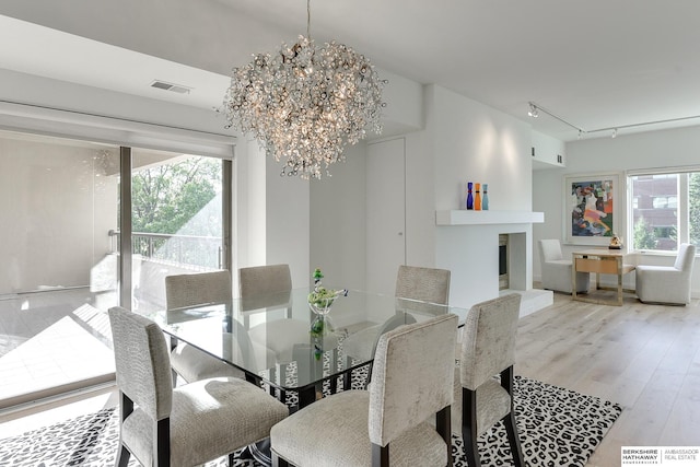 dining space featuring visible vents, track lighting, wood finished floors, a fireplace with raised hearth, and a chandelier
