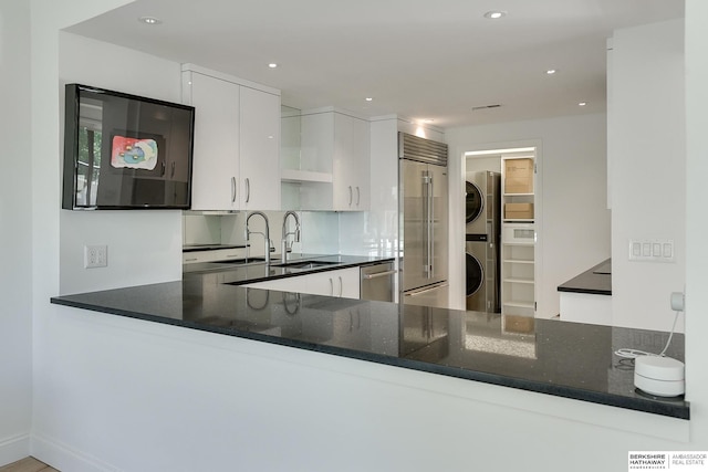 kitchen featuring a peninsula, stacked washer / dryer, recessed lighting, a sink, and appliances with stainless steel finishes