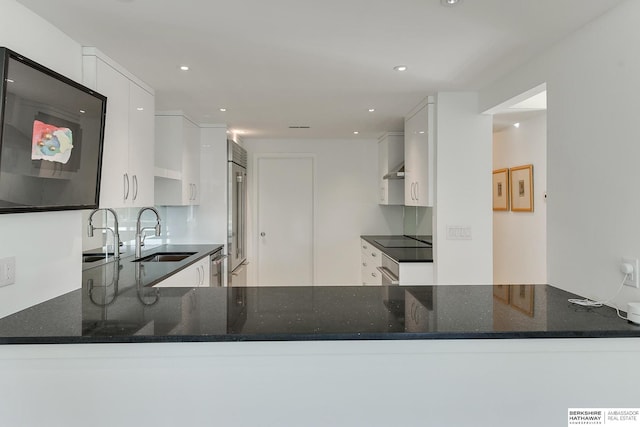 kitchen with white cabinets, appliances with stainless steel finishes, a sink, dark stone counters, and a peninsula