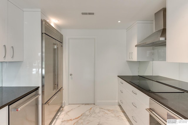 kitchen with dark countertops, appliances with stainless steel finishes, wall chimney exhaust hood, and marble finish floor