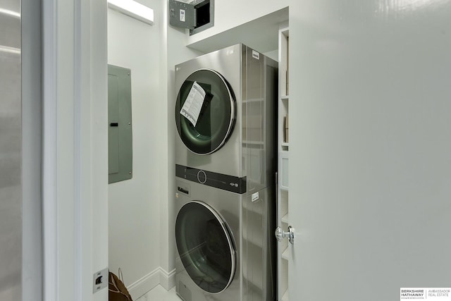 washroom featuring baseboards, stacked washing maching and dryer, and electric panel