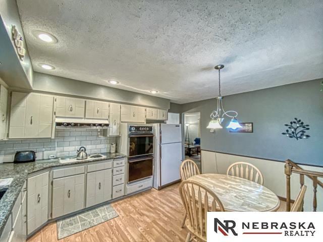 kitchen with light wood-style floors, a textured ceiling, dobule oven black, freestanding refrigerator, and cooktop