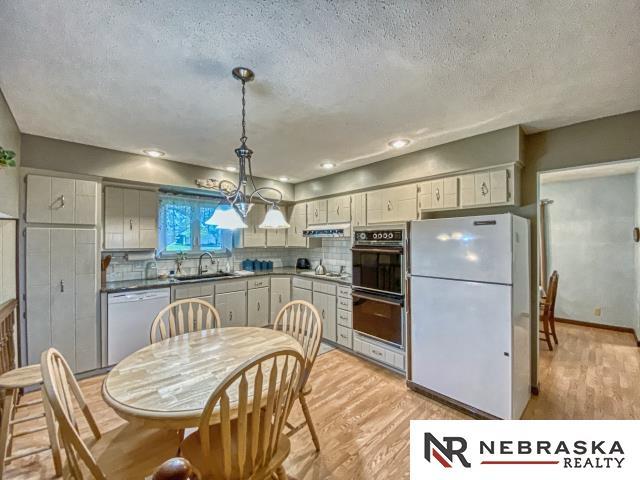 kitchen with white appliances, a textured ceiling, a sink, and light wood finished floors