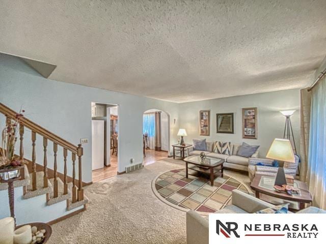 living area featuring light carpet, arched walkways, a textured ceiling, visible vents, and stairway