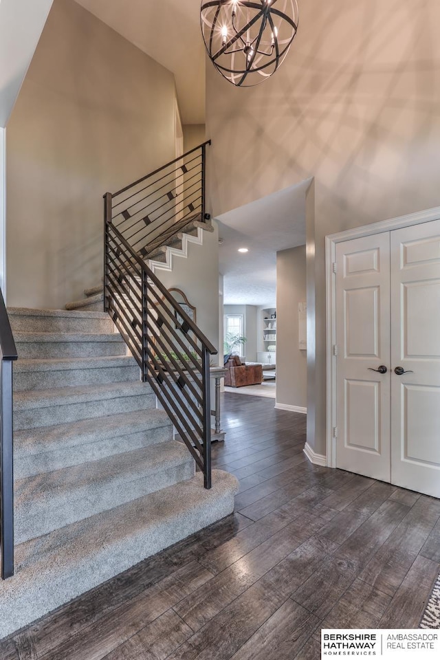 stairway with baseboards, a high ceiling, hardwood / wood-style flooring, and a chandelier
