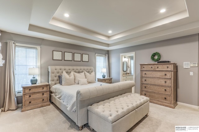 bedroom with recessed lighting, light colored carpet, ensuite bathroom, and a raised ceiling