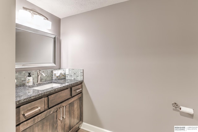 bathroom with vanity, a textured ceiling, baseboards, and tasteful backsplash