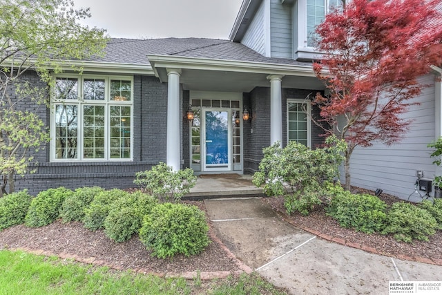 property entrance featuring a porch, brick siding, and roof with shingles