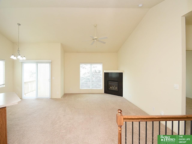 carpeted living room featuring a glass covered fireplace, a healthy amount of sunlight, vaulted ceiling, and ceiling fan with notable chandelier