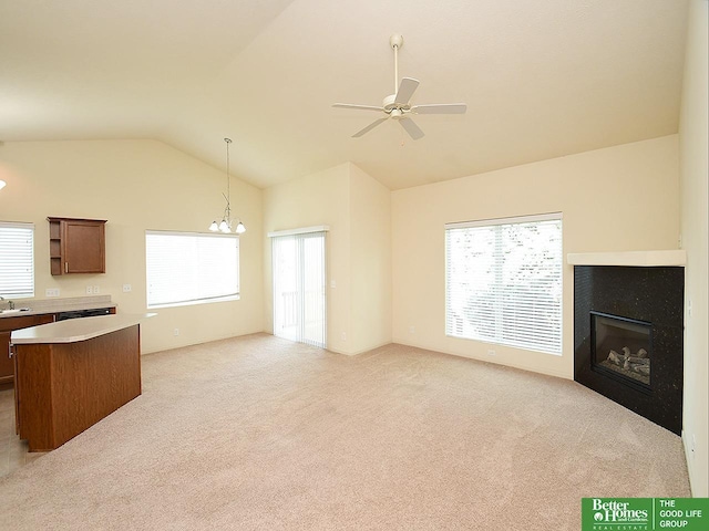 unfurnished living room featuring a sink, ceiling fan with notable chandelier, lofted ceiling, a glass covered fireplace, and light carpet