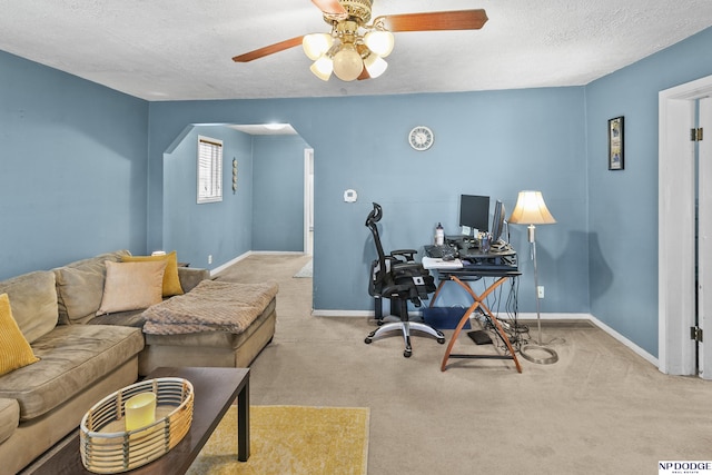 carpeted office with arched walkways, ceiling fan, baseboards, and a textured ceiling