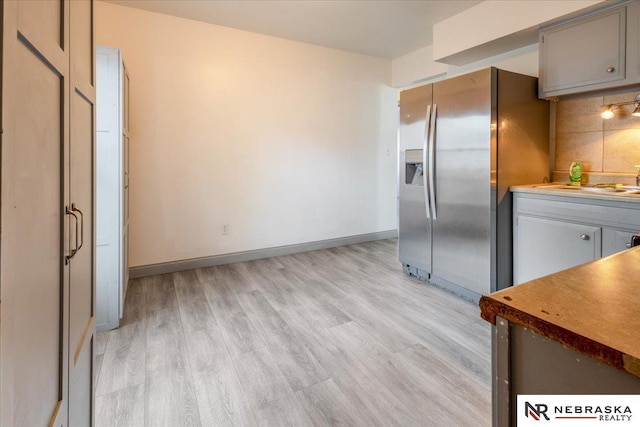 kitchen featuring stainless steel refrigerator with ice dispenser, tasteful backsplash, gray cabinets, and light wood-style floors