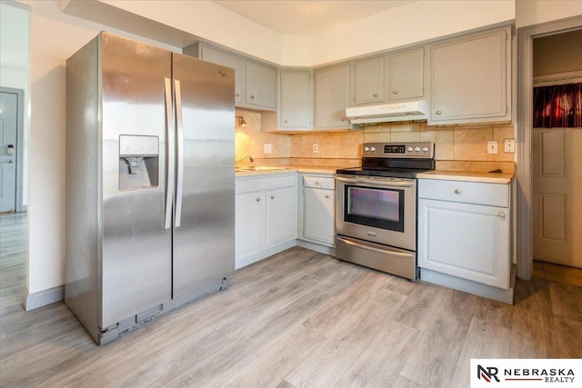 kitchen featuring appliances with stainless steel finishes, tasteful backsplash, light wood-type flooring, light countertops, and under cabinet range hood