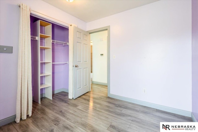 unfurnished bedroom with baseboards, wood finished floors, and a closet
