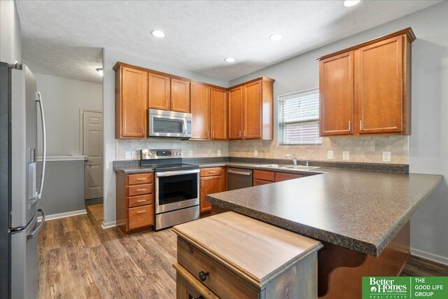 7714 S 167th St, Omaha, NE 68136 - kitchen with dark countertops, a sink, stainless steel appliances, a peninsula, and wood finished floors