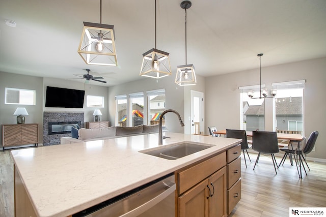 kitchen featuring a stone fireplace, decorative light fixtures, stainless steel dishwasher, a sink, and light wood-style flooring