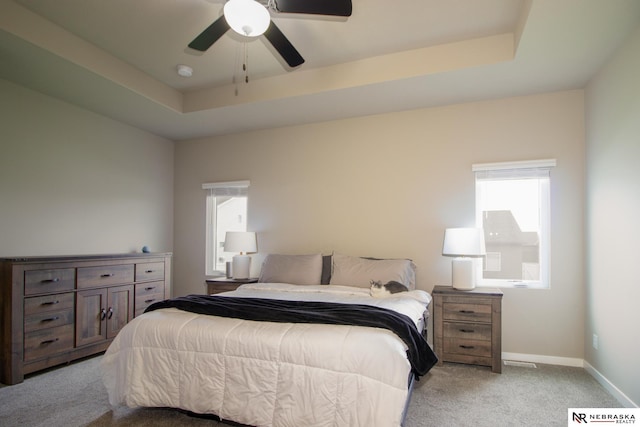 bedroom with light colored carpet, a ceiling fan, baseboards, and a tray ceiling