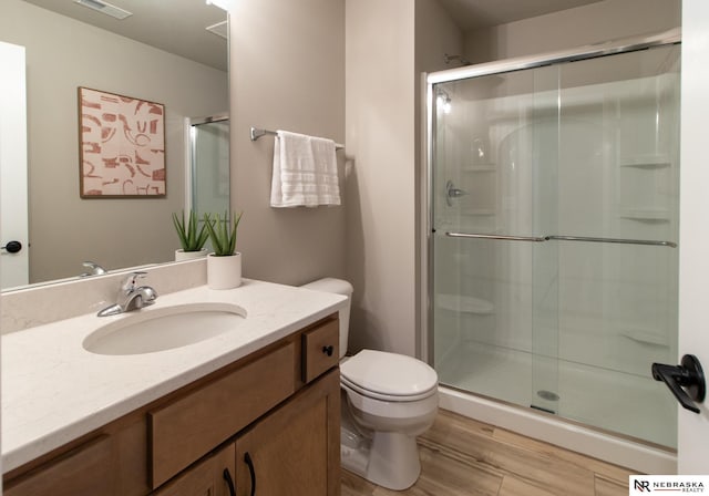 bathroom featuring vanity, wood finished floors, toilet, and a shower stall