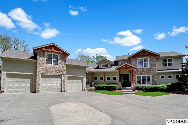 craftsman-style house featuring roof with shingles, an attached garage, driveway, and stone siding