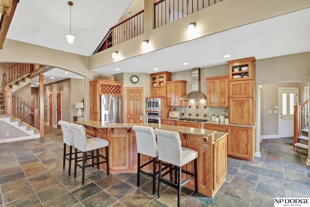 kitchen featuring arched walkways, appliances with stainless steel finishes, stone tile floors, and wall chimney range hood