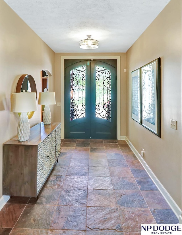 foyer featuring baseboards, french doors, a textured ceiling, and stone tile floors