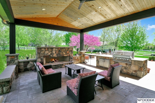 view of patio / terrace with fence, area for grilling, a grill, and an outdoor stone fireplace