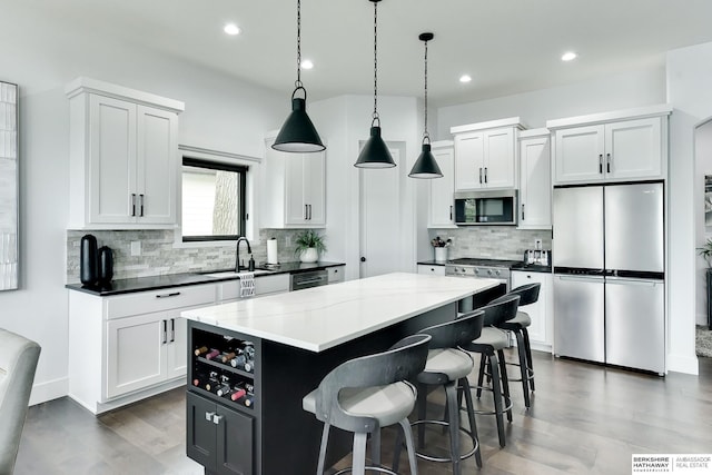 kitchen with wood finished floors, a center island, tasteful backsplash, a sink, and appliances with stainless steel finishes
