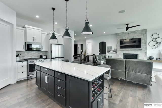 kitchen featuring a breakfast bar area, a kitchen island, a ceiling fan, wood finished floors, and stainless steel appliances