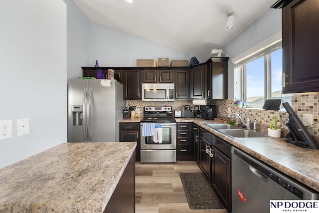 kitchen with a sink, stainless steel appliances, lofted ceiling, light wood-type flooring, and backsplash