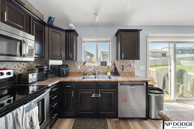 kitchen featuring appliances with stainless steel finishes, tasteful backsplash, light wood-type flooring, a sink, and light countertops