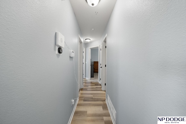 hall with baseboards, visible vents, and light wood-type flooring