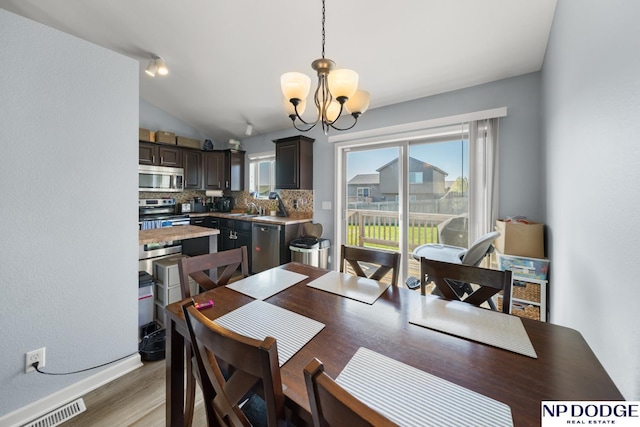 dining area with an inviting chandelier, light wood finished floors, a wealth of natural light, and visible vents