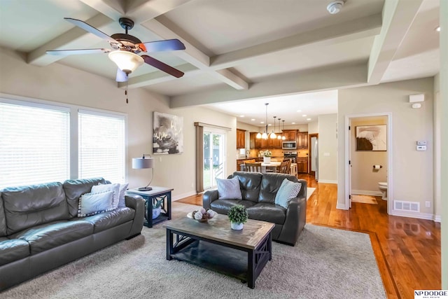 living room with ceiling fan with notable chandelier, baseboards, wood finished floors, beamed ceiling, and visible vents