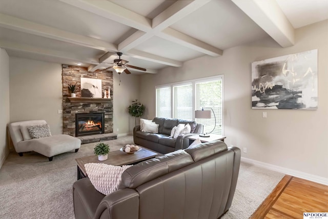 living area with a ceiling fan, baseboards, a stone fireplace, and beam ceiling