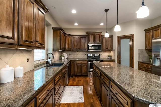 kitchen featuring dark wood-style flooring, dark stone counters, a sink, appliances with stainless steel finishes, and backsplash