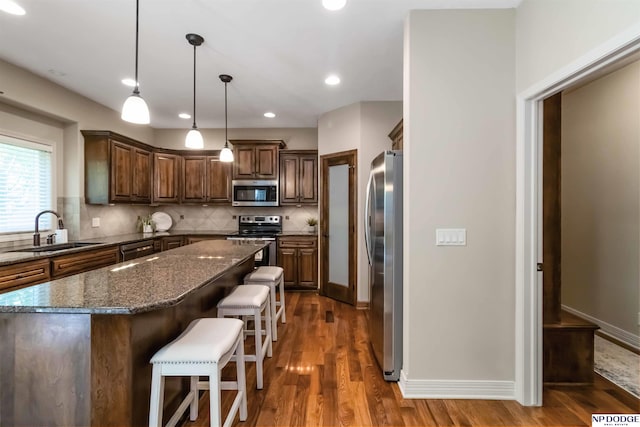 kitchen with dark wood-style flooring, appliances with stainless steel finishes, a breakfast bar, a sink, and decorative backsplash