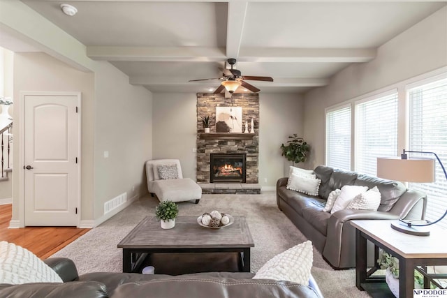 living room featuring beam ceiling, a stone fireplace, a ceiling fan, baseboards, and visible vents