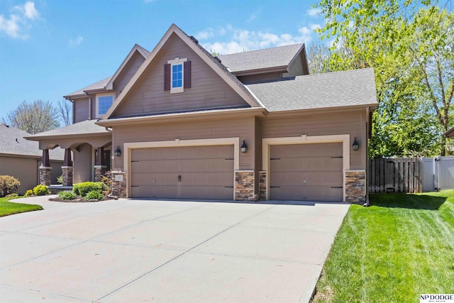 craftsman inspired home featuring fence, stone siding, a front yard, an attached garage, and driveway