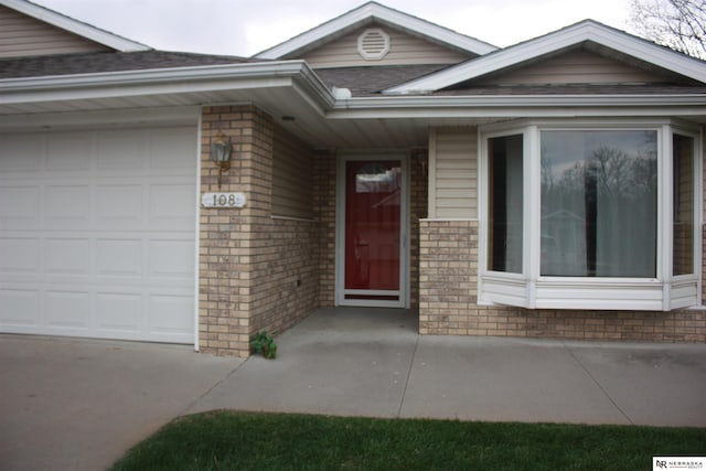 view of exterior entry featuring an attached garage, brick siding, and concrete driveway