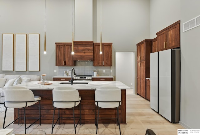 kitchen with a high ceiling, a sink, light countertops, freestanding refrigerator, and backsplash